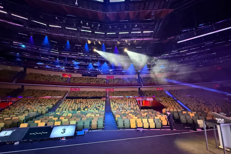 The view from the stage across the empty tiers of seating in a large auditorium, with stage lighting overhead, before the audience arrived